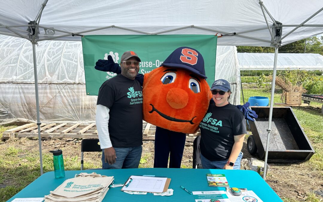 Image of Tim, Otto the Orange, and Maura standing behind the SOFSA table at the Brady Farm during On Farm Fest